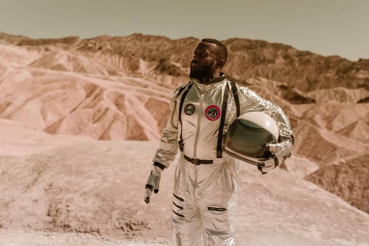 A man in a spacesuit explores a rocky desert, resembling an alien planet's surface.
