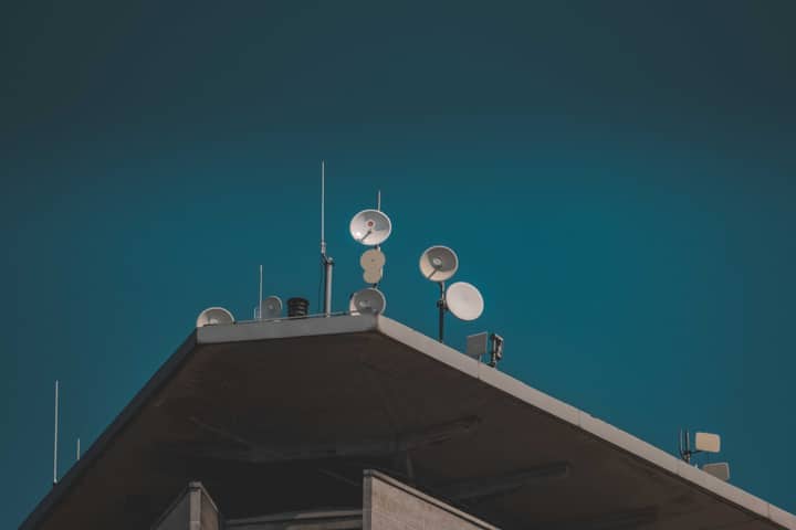A low-angle view of communication dishes and antennas on a building against a clear blue sky.