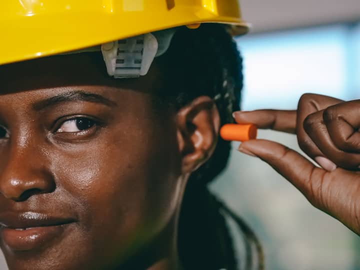 Close-up of a woman wearing a hard hat and fitting earplugs for safety on site.