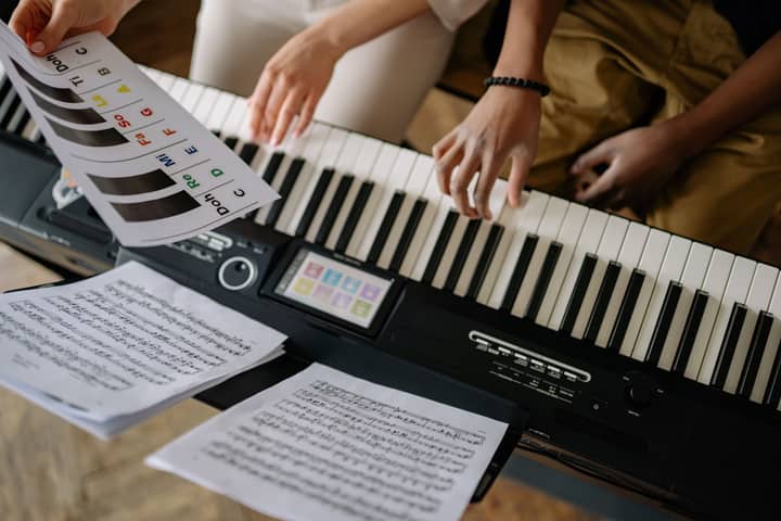 Hands on piano keyboard with sheet music, depicting a musical lesson in progress.