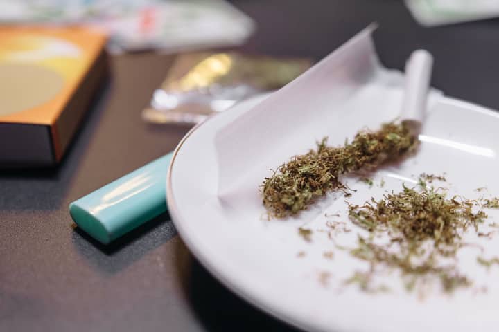A close-up view of cannabis being prepared for rolling with a lighter and ceramic plate.