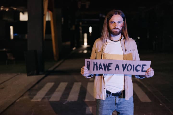 Man protesting at night holding "Have a Voice" sign, advocating for equality.