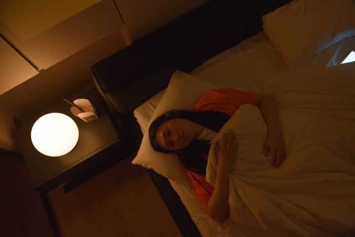 An Asian woman lies awake in bed under dim lighting, illustrating insomnia at night.