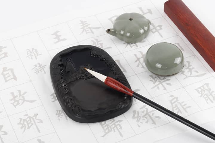 Flat lay of a traditional calligraphy set with ink stone, brush, and worksheet showcasing Chinese characters.