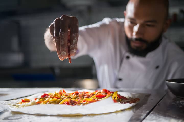 Professional chef skillfully preparing a vibrant homemade pizza with fresh ingredients.