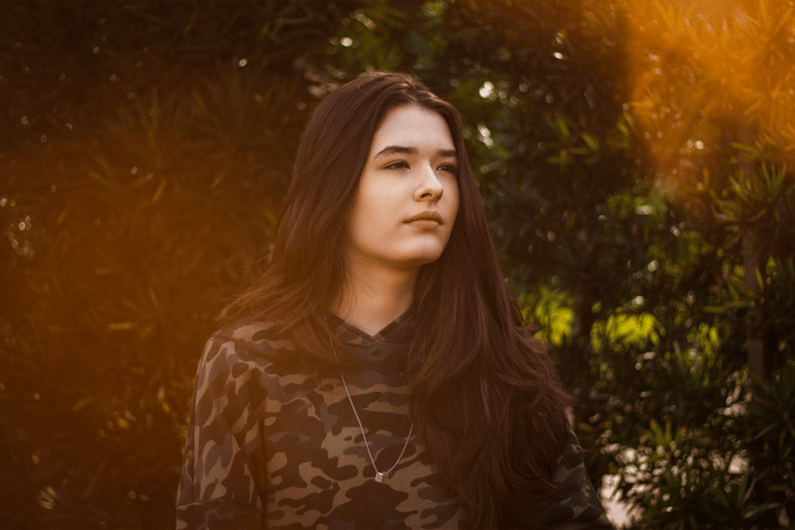 Portrait of a brunette woman in a camouflage shirt standing outdoors with natural sunlight.