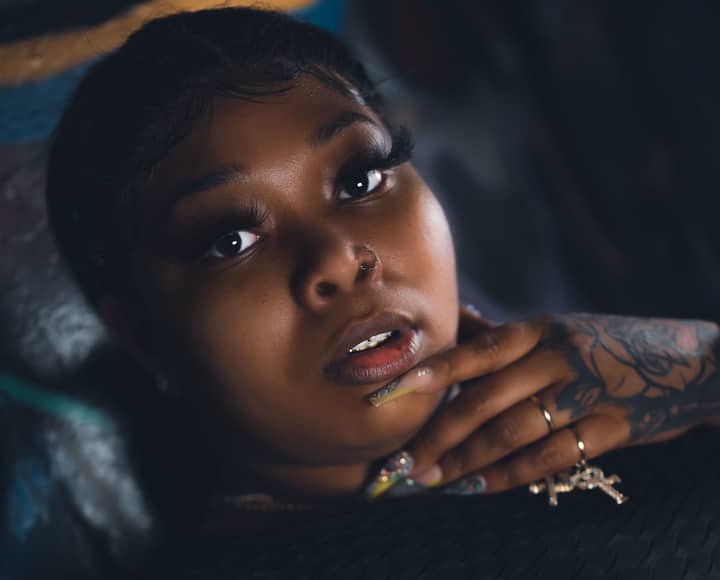 Close-up portrait of a tattooed woman with striking eyelashes and hand on chin, highlighting her beauty and expression.