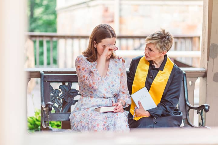 Woman receiving emotional support from a priest on a church bench.