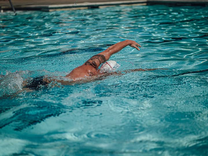 A tattooed swimmer practicing freestyle stroke in a sunlit swimming pool.