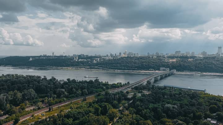A stunning aerial view of Kyiv's skyline and the Dnipro River, featuring a prominent bridge, amidst lush greenery.