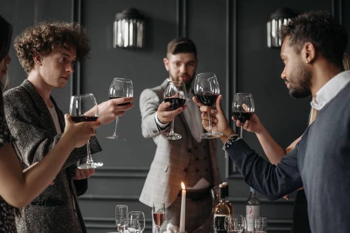 A group of elegantly dressed adults in suits toasting with red wine at a sophisticated party.