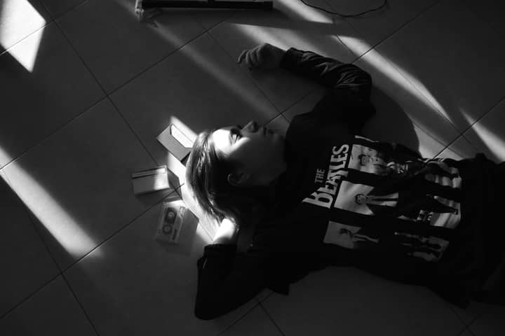 A woman in a Beatles shirt lies on the floor with cassette tapes in dramatic lighting.