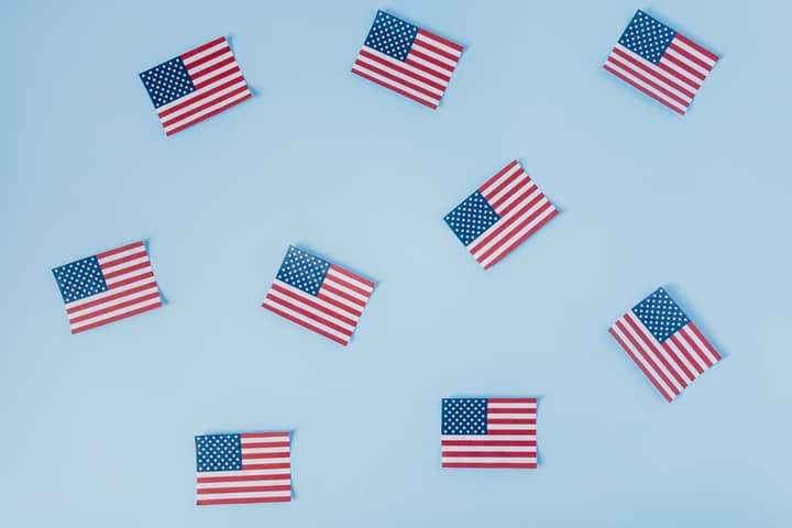 American flags scattered on a pastel blue background symbolizing patriotism and pride.