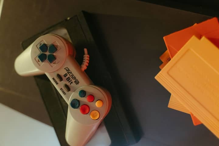 A vintage 8-bit game controller with colorful buttons next to classic game cartridges.