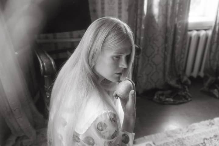 A vintage-style grayscale photo depicting a woman with long hair holding a fruit indoors.