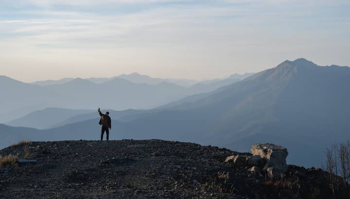 Silhouette of a person celebrating on a mountain summit at twilight with panoramic views.