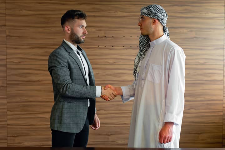 Two businessmen shaking hands indoors, symbolizing a successful cross-cultural partnership.
