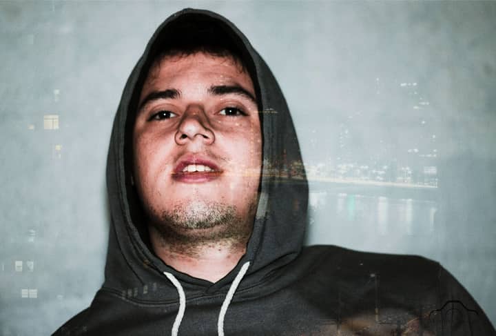 A creative double exposure portrait of a young man in a hoodie with city lights overlay.