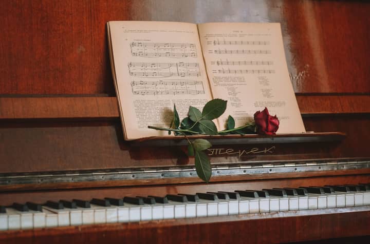 A close-up of piano keys with an open music book and a red rose, creating a romantic ambiance.
