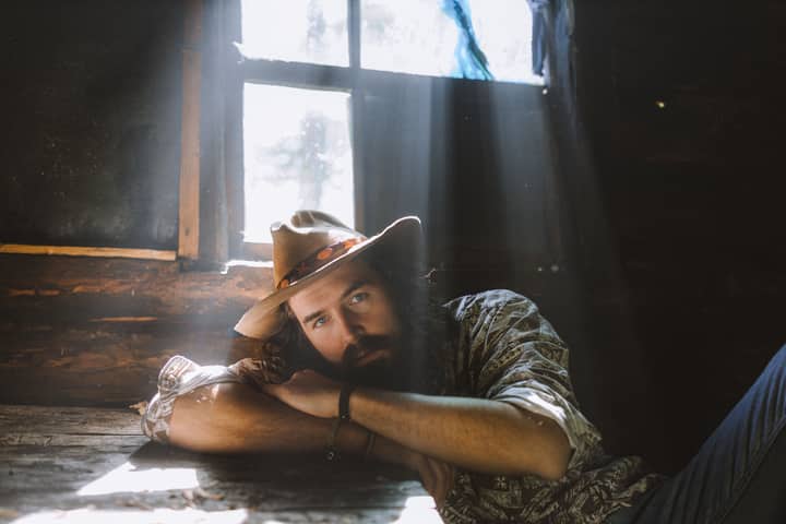Reflective man in a rustic cabin setting, bathed in dramatic natural light for a moody ambiance.