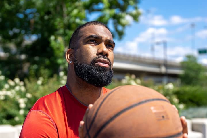 Close-up of a thoughtful man with a basketball against a sunny backdrop.