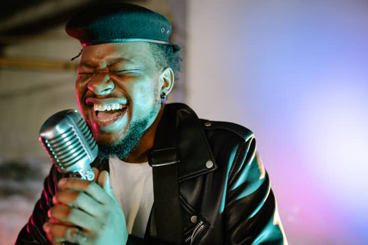 Dynamic portrait of an African American man passionately singing with a microphone under colorful stage lights.