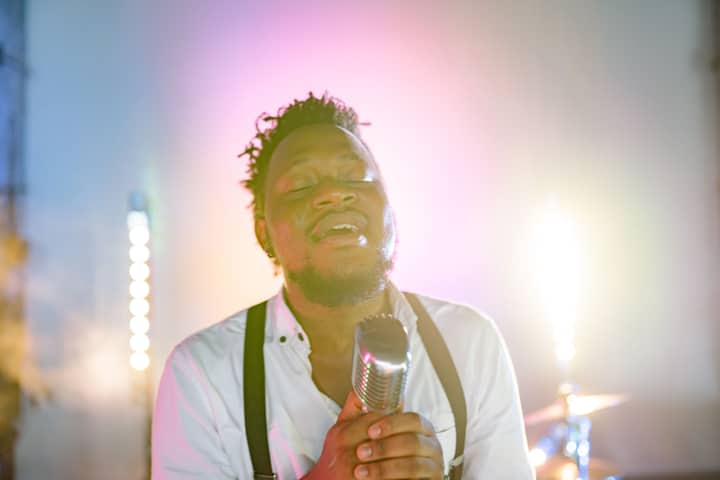 An African American man passionately singing into a retro microphone on stage.