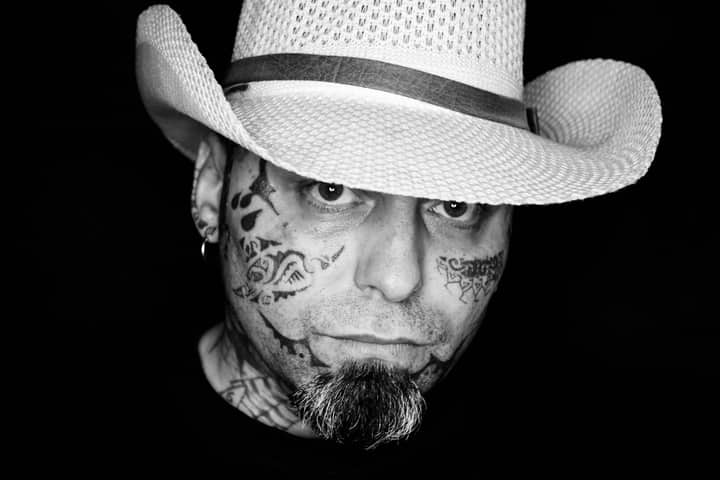 Close-up black and white portrait of a tattooed man wearing a cowboy hat.