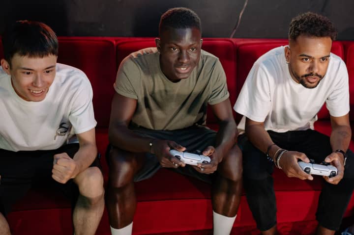 Three young men gaming on a sofa, showcasing diversity and fun.