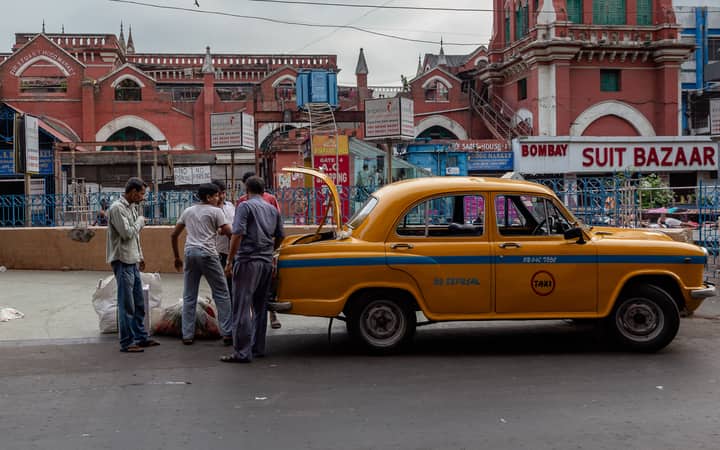 Street scene with a classic yellow taxi and people on a bustling city road.