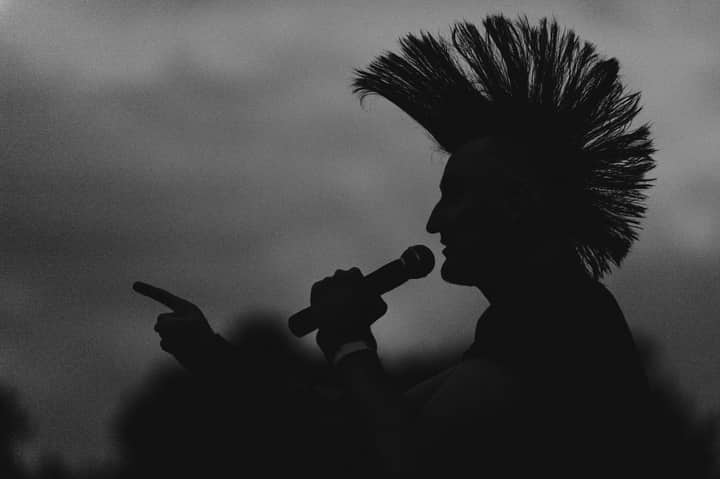 A striking silhouette of a punk singer pointing with a microphone under a dramatic sky.