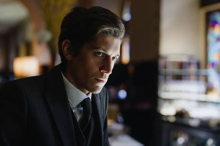 Close-up of a thoughtful man in a black suit in an elegant indoor setting.