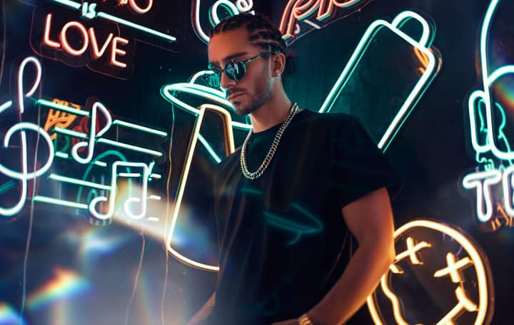 Cool urban portrait of a man wearing sunglasses and chain necklace amidst glowing neon signs.