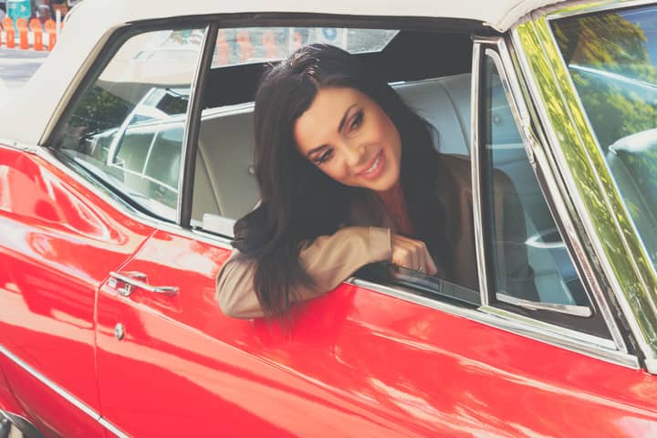 Woman sitting and smiling in a red classic cabriolet car.