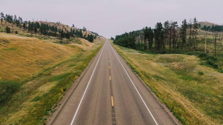 A long empty road through grassy fields and rolling hills, perfect for travel enthusiasts.