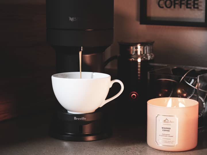 A coffee machine brewing a warm drink beside a scented candle, capturing a cozy atmosphere.