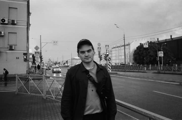 A black and white street portrait of a man standing on a city sidewalk.