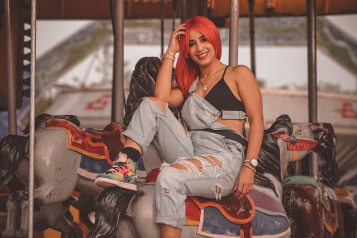 Vibrant woman with red hair sitting on a carousel horse at a carnival, showcasing playful fashion style.