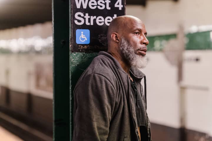 Elderly man standing thoughtfully at West 4th Street subway platform, conveying urban solitude.