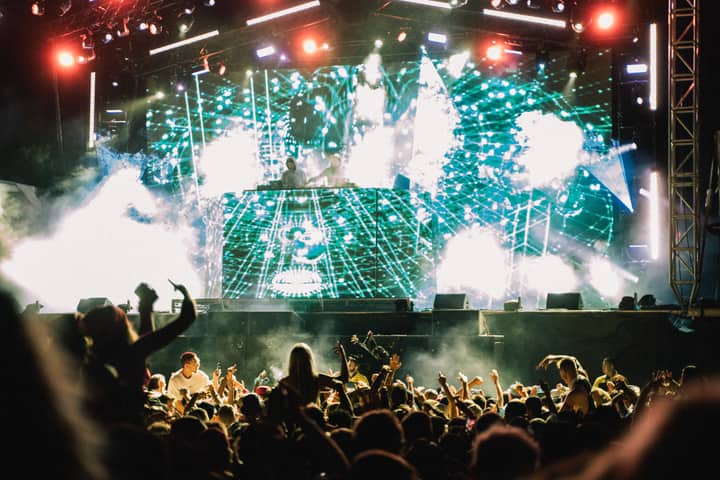 Vibrant music concert with DJ and crowd at night, showcasing lively atmosphere and dazzling lights.