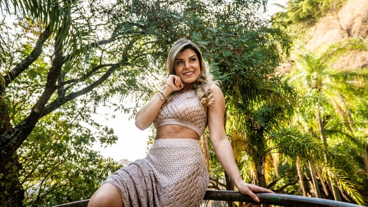Stylish woman in a crop top smiling amidst lush greenery on a sunny day.