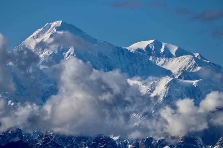 Stunning aerial view of the snow-covered Denali peak surrounded by clouds in Alaska.