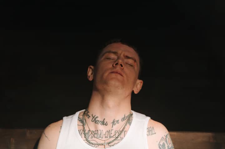 Intimate portrait of a tattooed man with eyes closed, exuding a punk vibe in dim lighting.