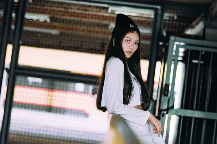 Stylish young Asian woman posing confidently in a modern urban setting with long sleeves and a beanie.