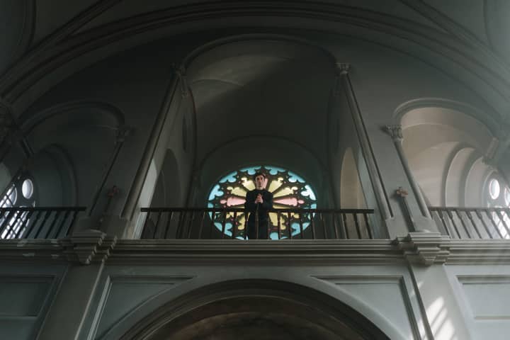 A priest stands at the altar in an ornate church with beautiful arches and stained glass.