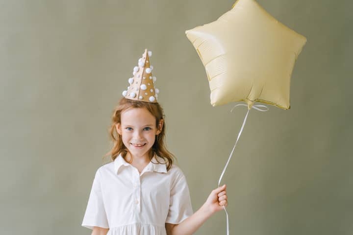 Smiling girl with party hat and star balloon, enjoying a fun birthday celebration.