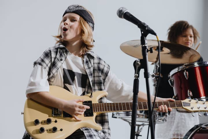 Young musicians passionately playing electric guitar and drums on stage, showcasing kids' musical talent.