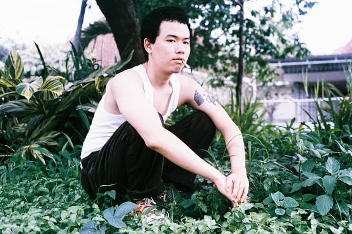 A young man in a garden, crouching with a cigarette, conveys a relaxed lifestyle vibe.