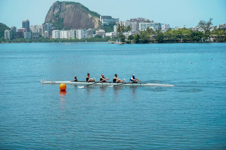 A team of rowers paddling on a serene lake in Rio de Janeiro with iconic landscape in the background.
