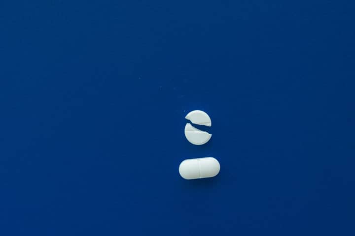Close-up of a broken and whole white pill on a blue background, representing medication and health concepts.